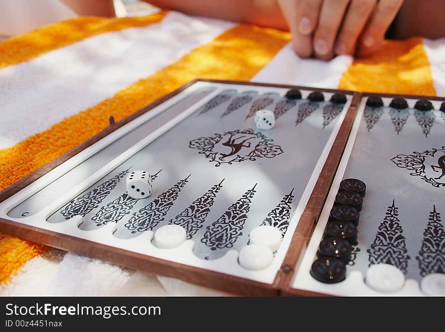 Open board of backgammon is laying on striped towel. Open board of backgammon is laying on striped towel