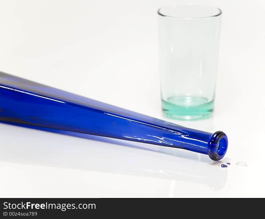 Blue bottle and a green glass on reflective background