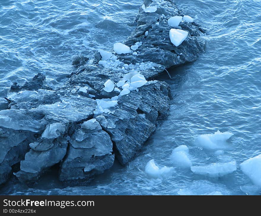 Glacier remnants floating past rock formation.