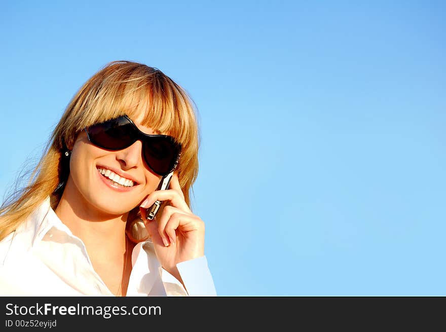 A beautiful young woman using a mobile phone on the sky background. A beautiful young woman using a mobile phone on the sky background