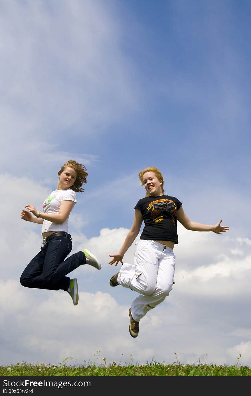 The two happy jumping girls on a background of the blue sky