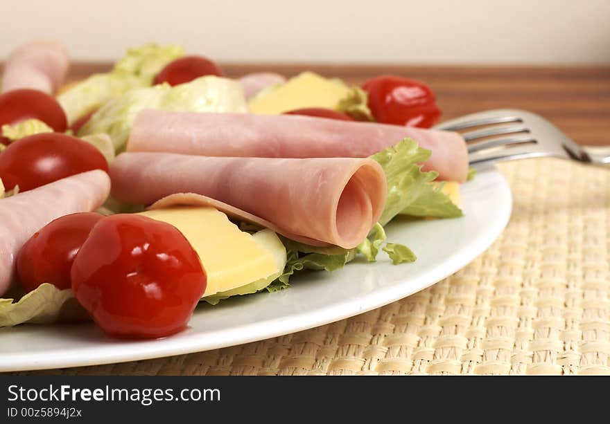 Fresh salad with cold meat, green lettuce leaves, white cheese, tomatoes and peppadew peppers on white plate. Fresh salad with cold meat, green lettuce leaves, white cheese, tomatoes and peppadew peppers on white plate