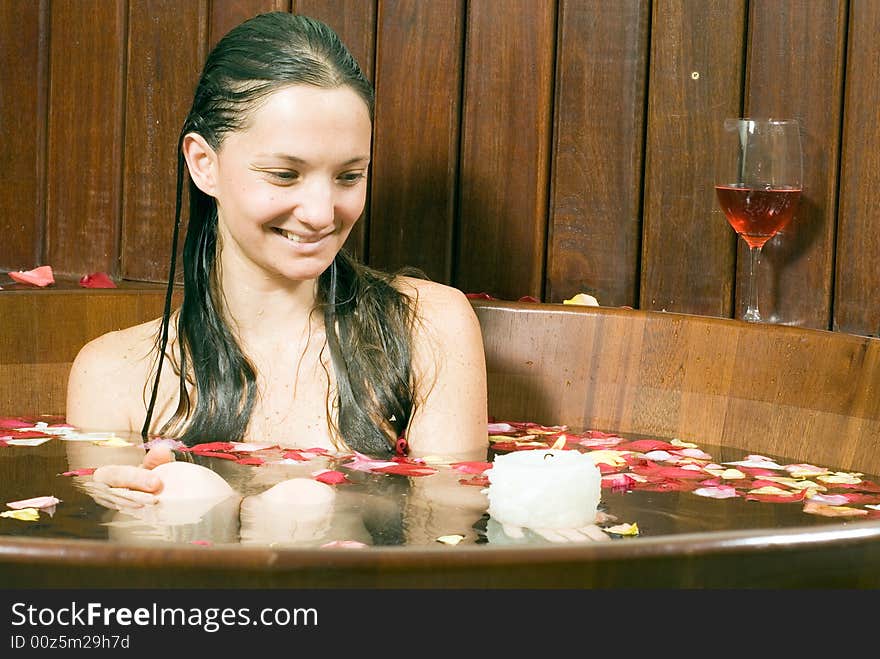 Woman smiles she looks at a candle. She is relaxing in a spa tub filled with flowers. Horizontally framed photograph. Woman smiles she looks at a candle. She is relaxing in a spa tub filled with flowers. Horizontally framed photograph.