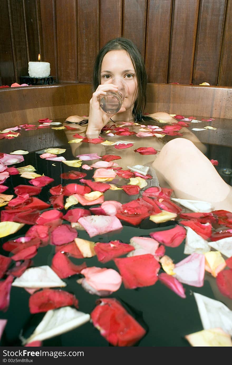 Woman sips water as she lounges in a spa tub filled with flower petals. Vertically framed photograph. Woman sips water as she lounges in a spa tub filled with flower petals. Vertically framed photograph.