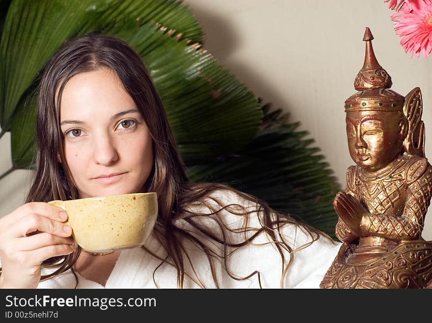 Woman holds a tea cup. She sits next to a bronze statue. Horizontally framed photograph. Woman holds a tea cup. She sits next to a bronze statue. Horizontally framed photograph.