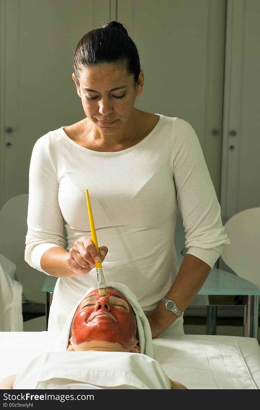 A relaxed smiling woman getting a red facial mask brushed on at a spa.  Vertically framed shot. A relaxed smiling woman getting a red facial mask brushed on at a spa.  Vertically framed shot.