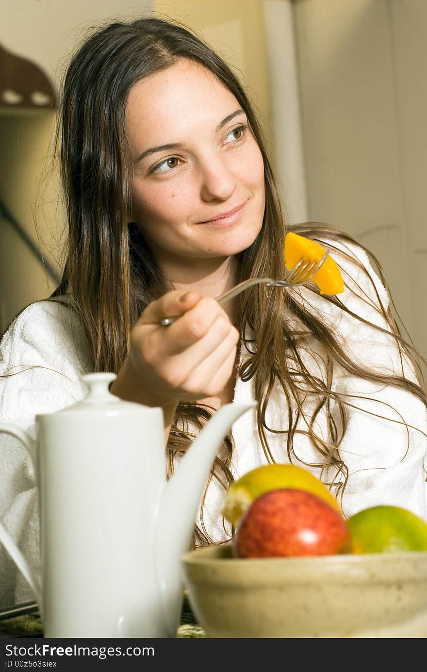 Woman smiles as she has breakfast. There is fruit and tea on the table. Vertically framed photograph. Woman smiles as she has breakfast. There is fruit and tea on the table. Vertically framed photograph.