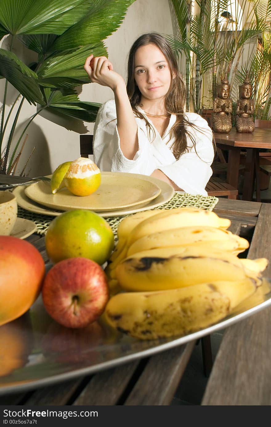 Woman smiles as she has breakfast. There are many fruits on the table. Vertically framed photograph. Woman smiles as she has breakfast. There are many fruits on the table. Vertically framed photograph.