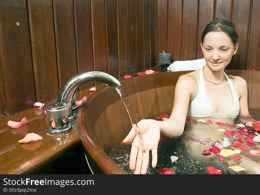 Woman relaxes in a spa tub filled with flowers and holds her hand under a faucet. Horizontally framed photograph. Woman relaxes in a spa tub filled with flowers and holds her hand under a faucet. Horizontally framed photograph