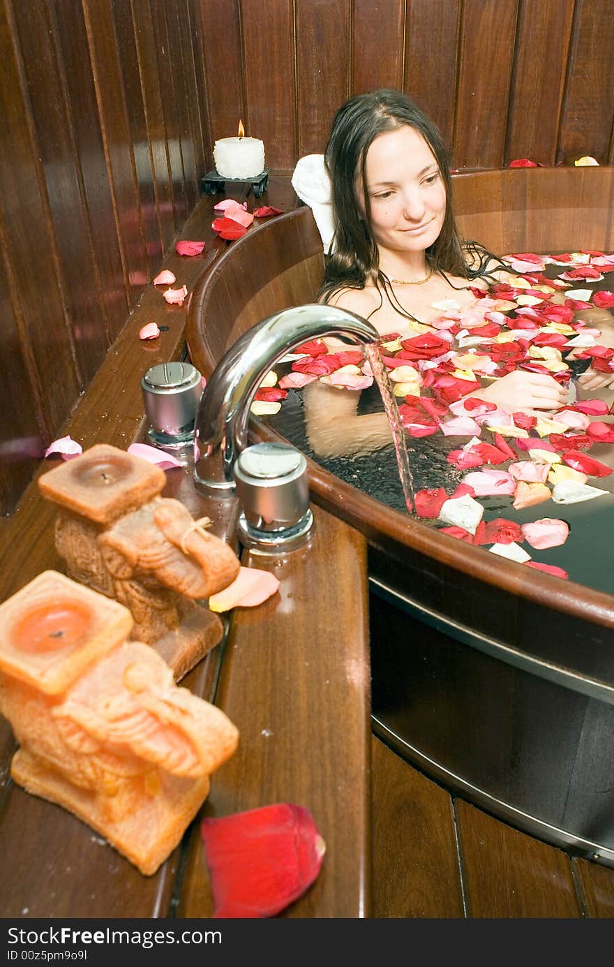 Woman relaxes in a spa tub filled with flowers and smiles.. Vertically framed photograph. Woman relaxes in a spa tub filled with flowers and smiles.. Vertically framed photograph