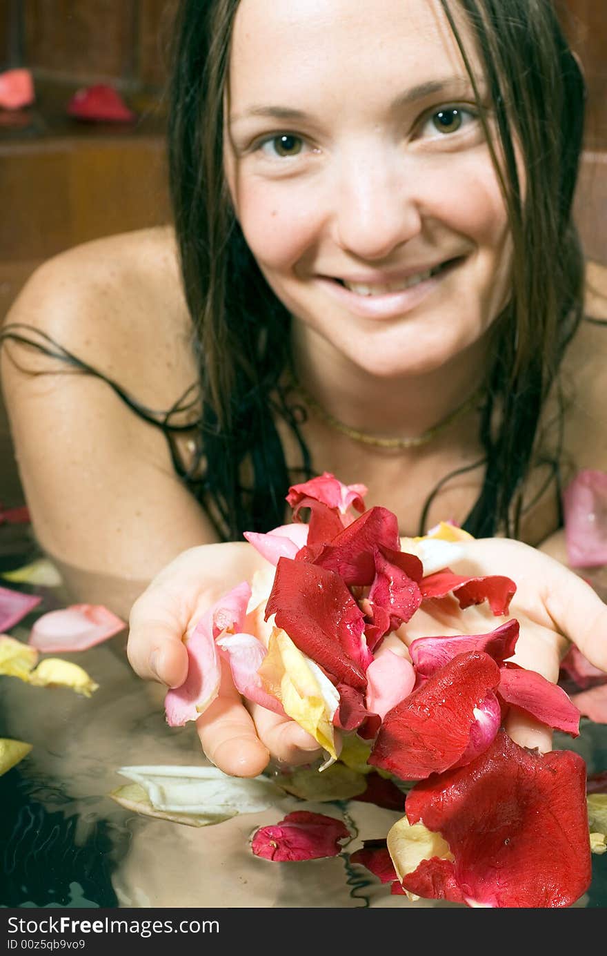 Woman smiles as she scoops up flower petals in her hands while she bathes. Vertically framed photograph. Woman smiles as she scoops up flower petals in her hands while she bathes. Vertically framed photograph.