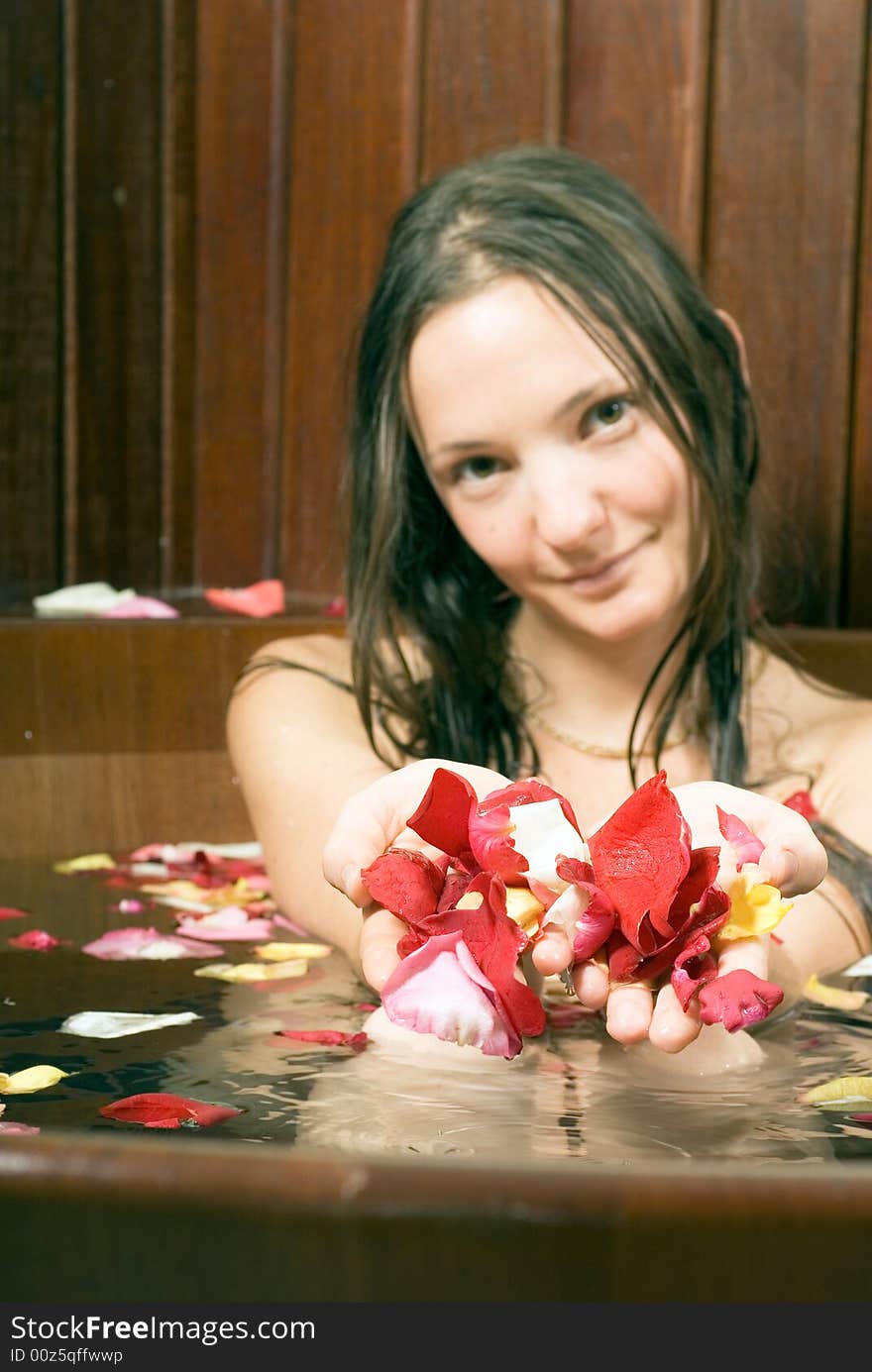 An attractive young lady holding multi-colored rose petals while sitting in a bathtub full of water. Vertically framed shot. An attractive young lady holding multi-colored rose petals while sitting in a bathtub full of water. Vertically framed shot.