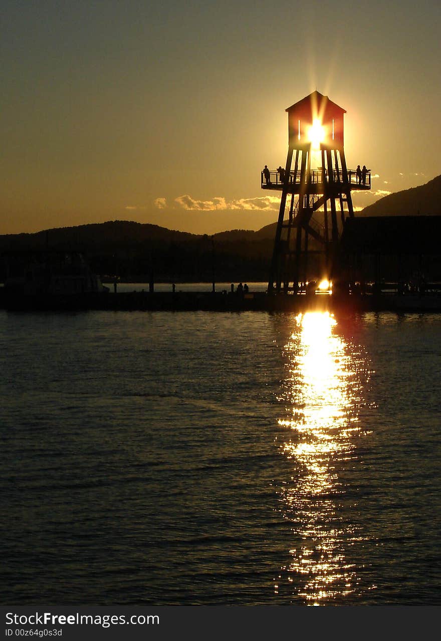 Observation tower in silhouette at sunset on Memphremagog lake in Magog, province of Quebec, Canada, with Mont-Orford in background. Observation tower in silhouette at sunset on Memphremagog lake in Magog, province of Quebec, Canada, with Mont-Orford in background