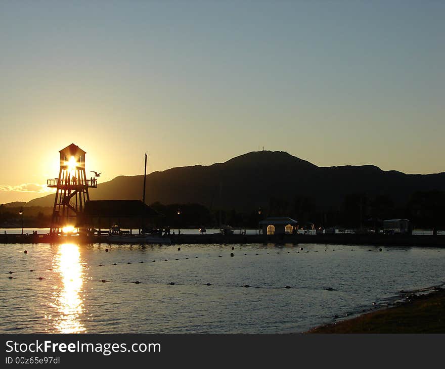 Observation tower in silhouette at sunset on Memphremagog lake, province of Quebec, Canada, with Mont-Orford in background. Observation tower in silhouette at sunset on Memphremagog lake, province of Quebec, Canada, with Mont-Orford in background