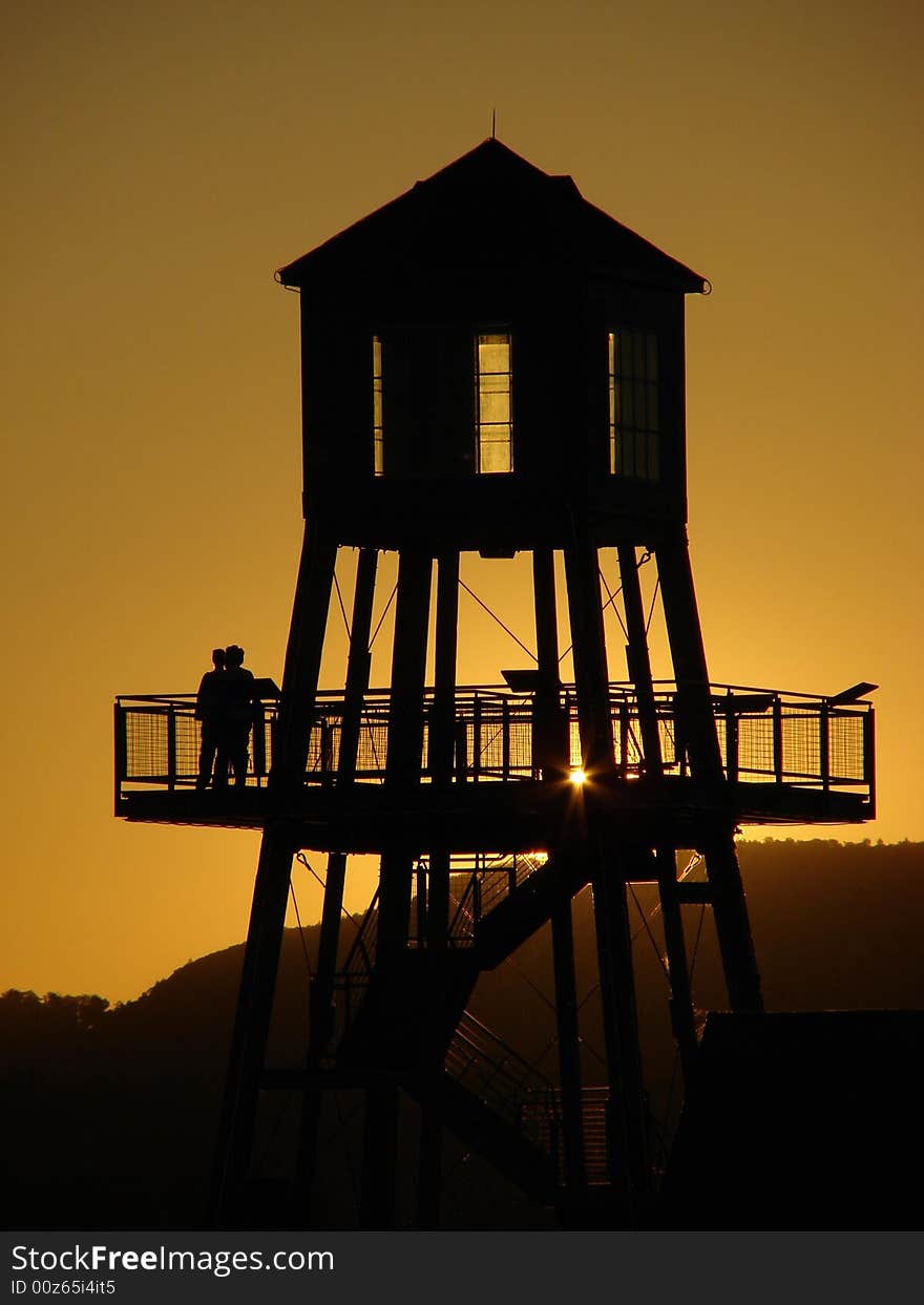 Observation tower in silhouette at sunset on Memphremagog lake in Magog, province of Quebec, Canada, with Mont-Orford in background. Observation tower in silhouette at sunset on Memphremagog lake in Magog, province of Quebec, Canada, with Mont-Orford in background