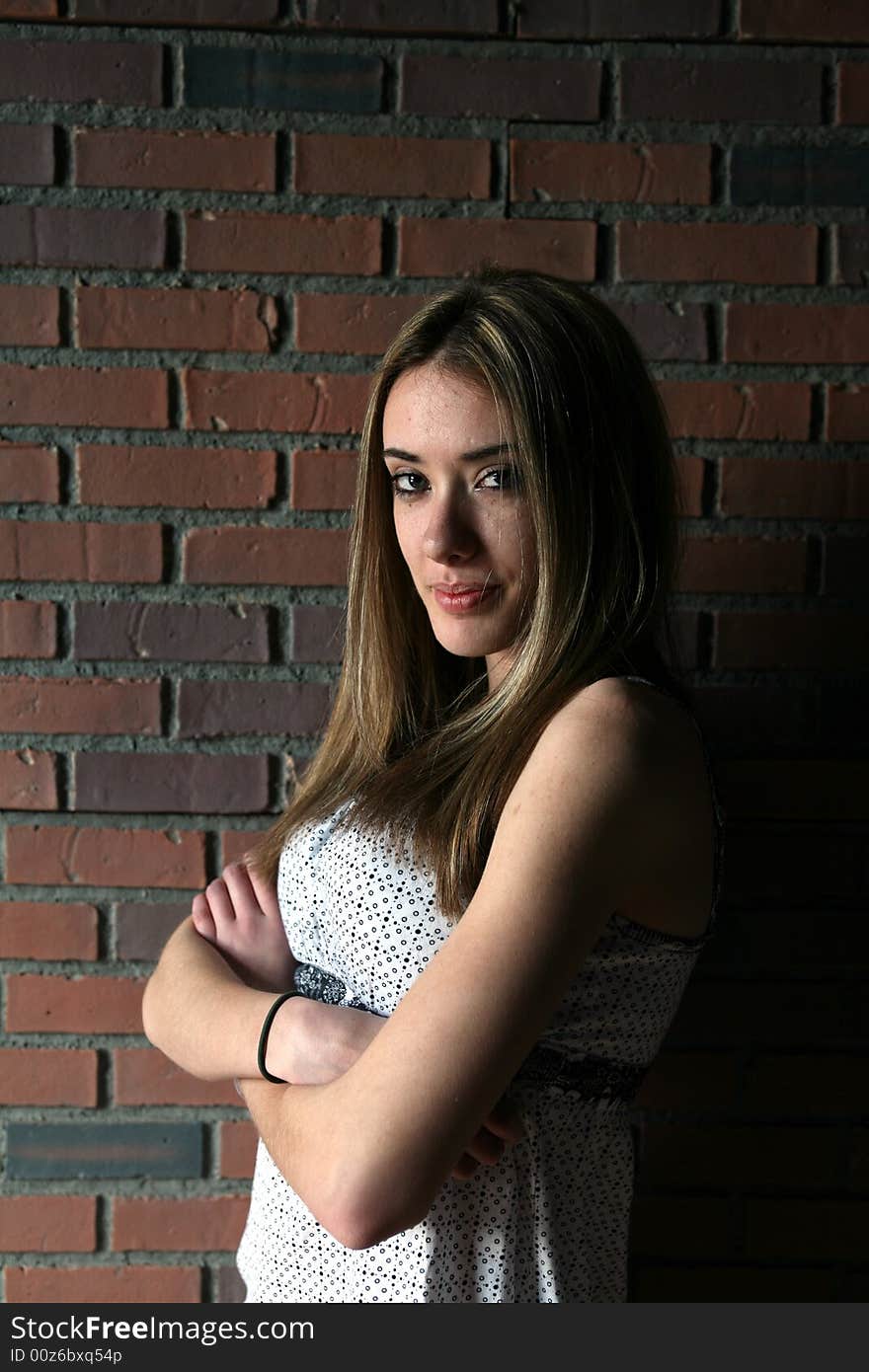 Pretty teenage girl with arms crossed; against a brick wall