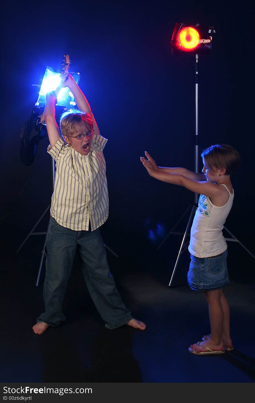 Big brother holding guitar up in the air and getting ready to smash it on his little sister, who has her hands out in defense.