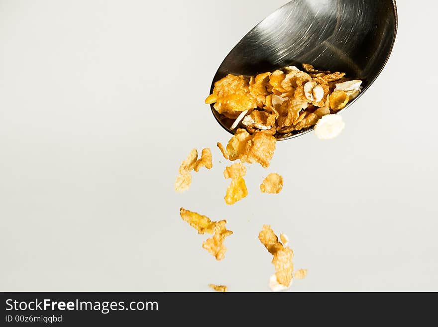 Cereals poured from a table spoon on grey background