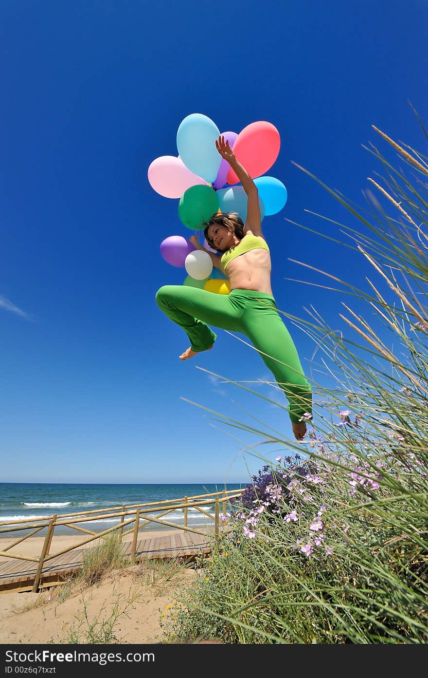 Girl with colorful balloons jumping on the beach