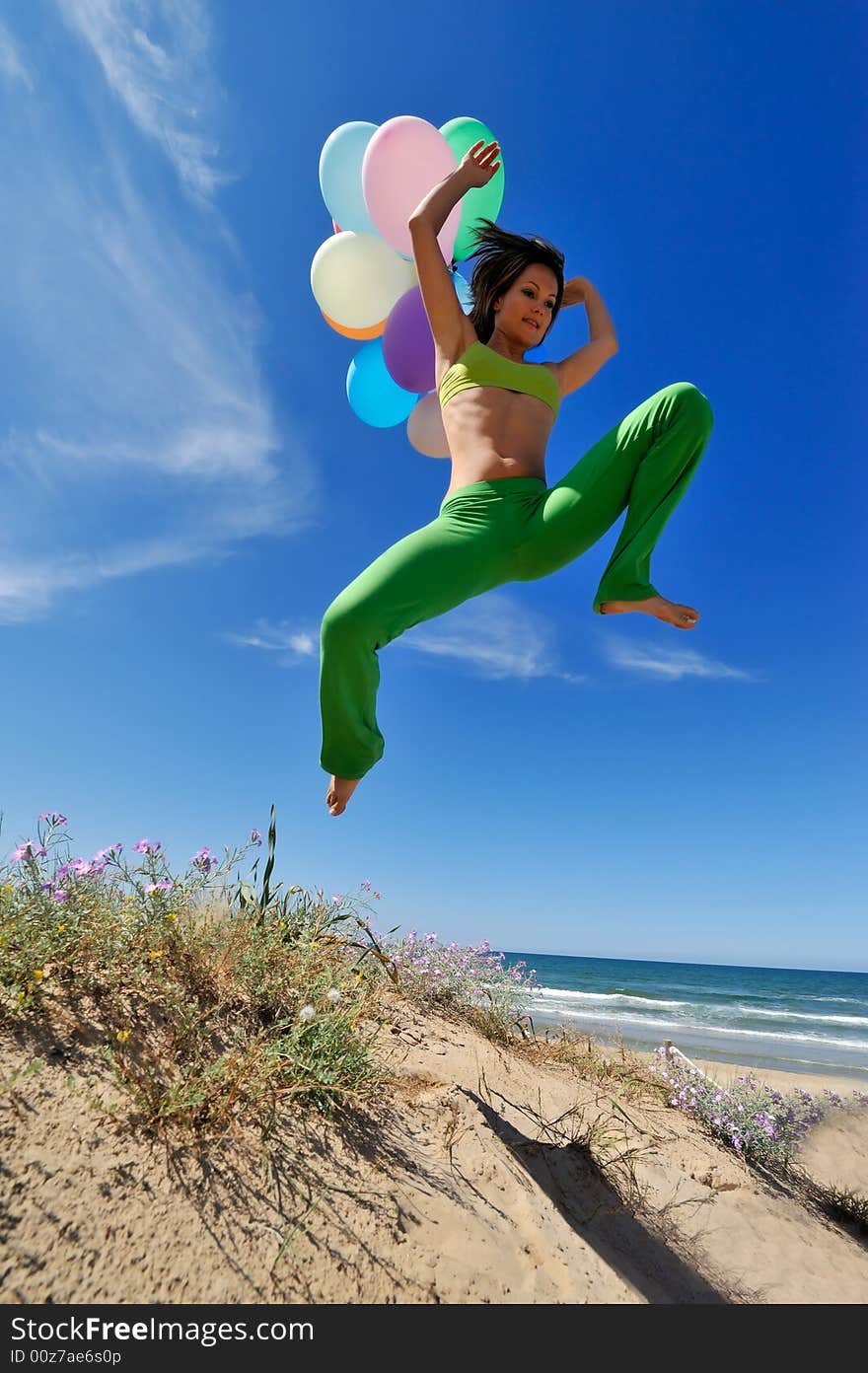 Girl with colorful balloons jumping on the beach