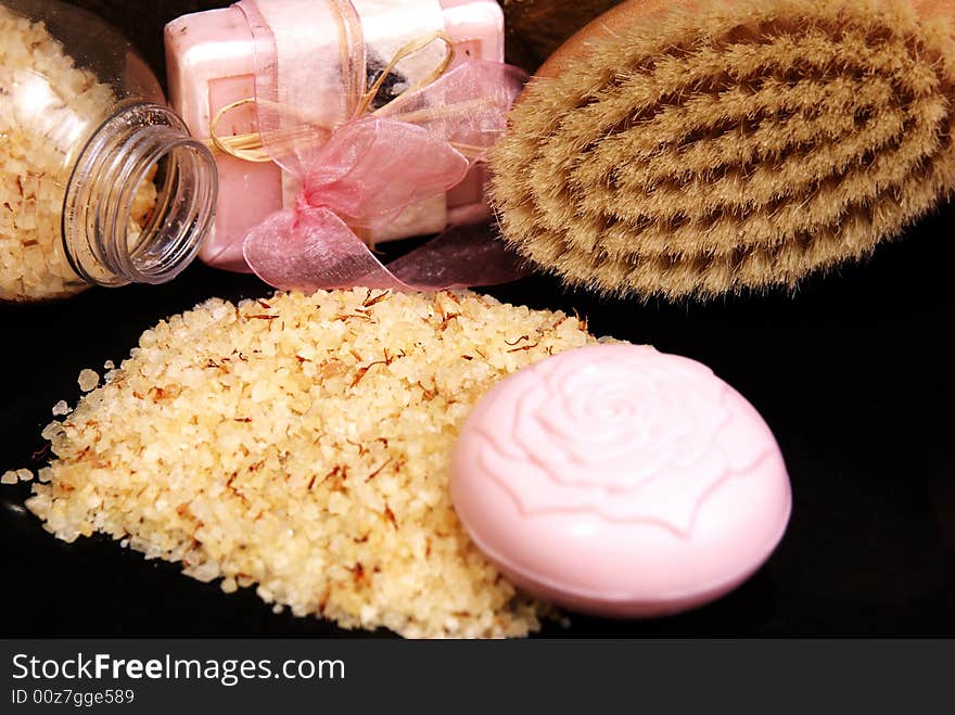 Bath salt and soap with a pink ribbon, with rose petals and bright orange towel laying on black granite. Bath salt and soap with a pink ribbon, with rose petals and bright orange towel laying on black granite