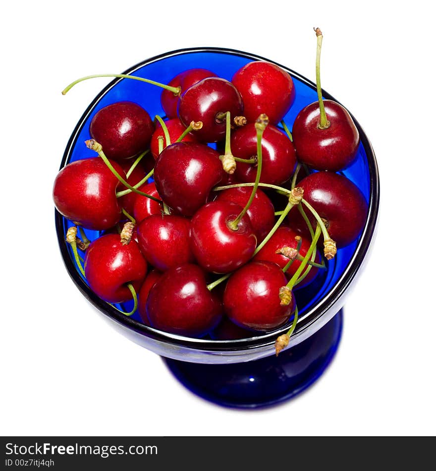 Ripe fresh sweet cherries in the cup of blue glass, isolated on white. Ripe fresh sweet cherries in the cup of blue glass, isolated on white