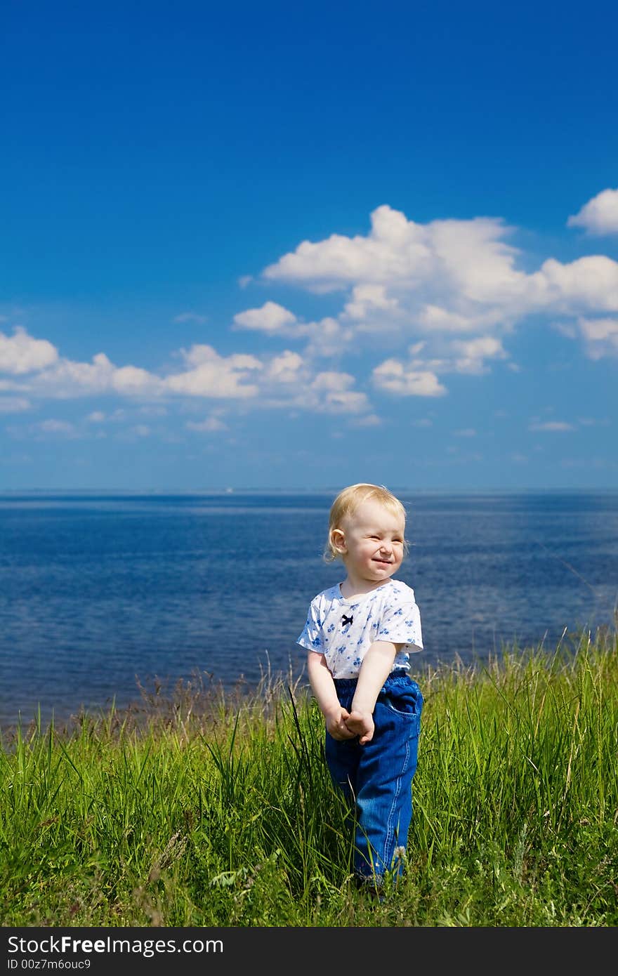 Small girl in green grass over the blue sky near the river. Small girl in green grass over the blue sky near the river