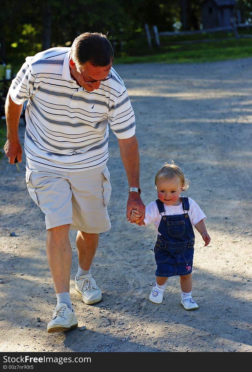 A grandfather guides his granddaughter down a country lane hand in hand. A grandfather guides his granddaughter down a country lane hand in hand