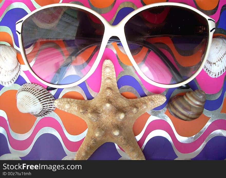 Solar glasses and different seashells on a shining and bright background