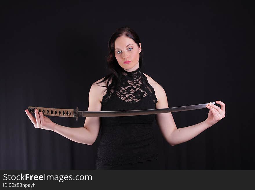 Young woman holding a samurai sword, katana, against black. Young woman holding a samurai sword, katana, against black