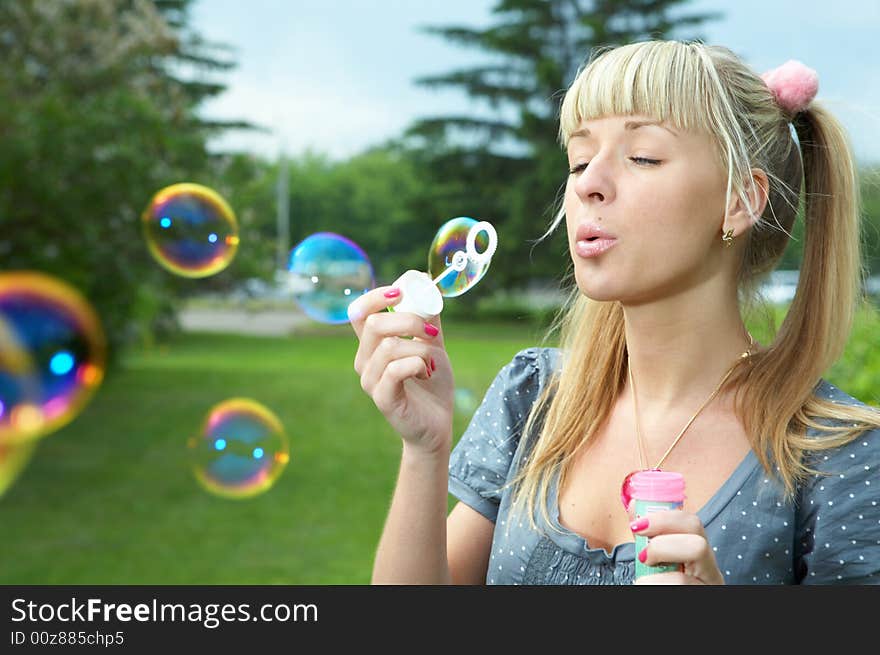 Young girl makes soap bubble on grass