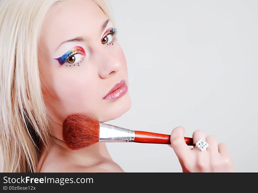 Beautiful girl with bright make-up, looks through a shoulder and holds a brush in a hand. Beautiful girl with bright make-up, looks through a shoulder and holds a brush in a hand