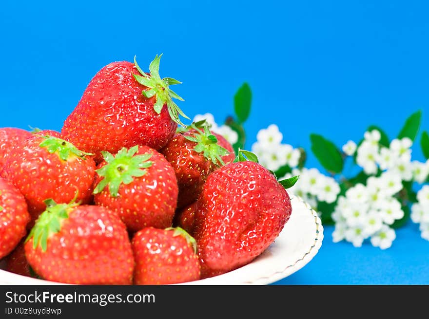 Fresh strawberries and flowers on blue background