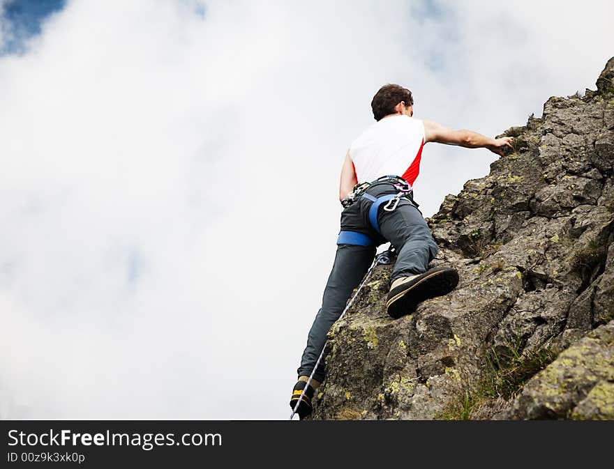 White young male rock-climber, summer season, upward view, horizontal frame, vibrant colours, copy-space on the left. White young male rock-climber, summer season, upward view, horizontal frame, vibrant colours, copy-space on the left