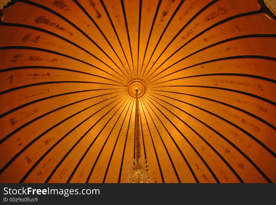 Close up on a round gold cupola ceiling, with a long chandelier