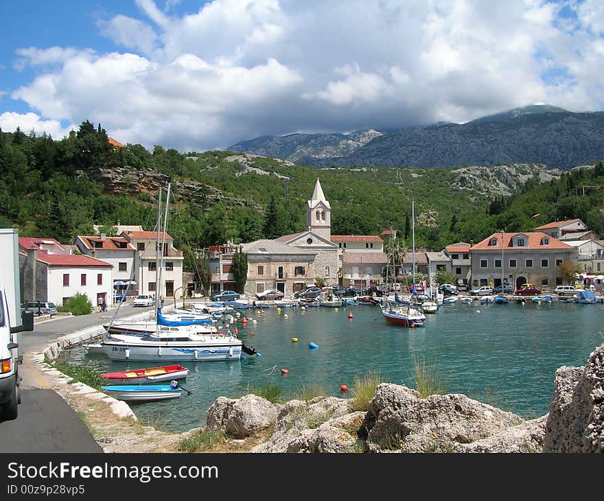 Small shipyard with small boats, mountains and clouded skies, old buildings, and roads. Small shipyard with small boats, mountains and clouded skies, old buildings, and roads