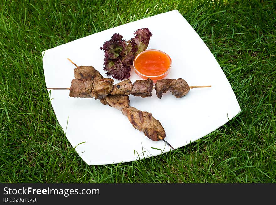 Dish of fresh kebabs on sticks with hot sauce, on green grass