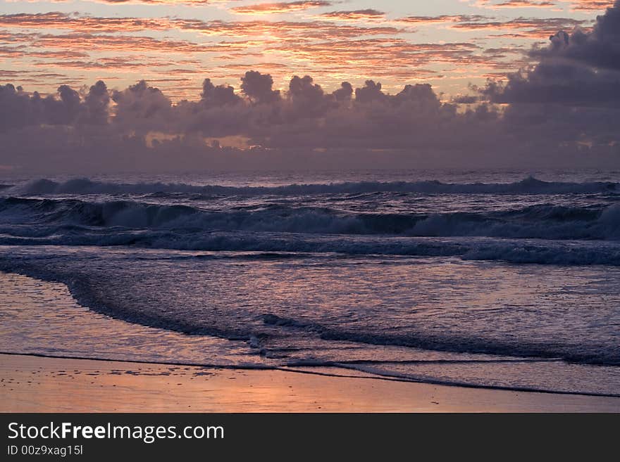 Sunset over a beautiful sandy beach, Very clear and bright perspective with clouds layers that accentuate the horizon, ocean waves are approachind the sandy beach. Sunset over a beautiful sandy beach, Very clear and bright perspective with clouds layers that accentuate the horizon, ocean waves are approachind the sandy beach