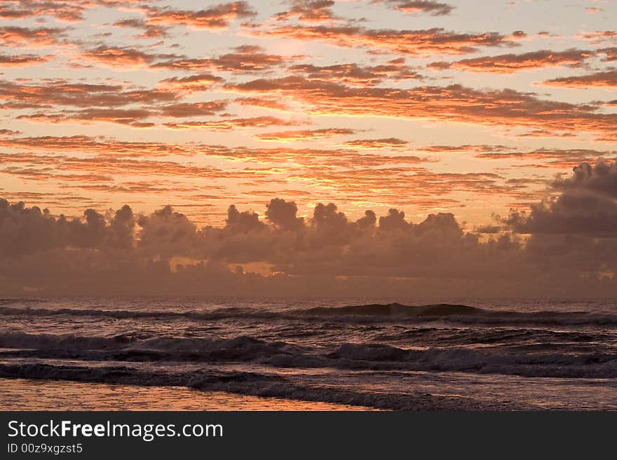 Sunset over a beautiful sandy beach, Very clear and bright perspective with clouds layers that accentuate the horizon, ocean waves are approachind the sandy beach. Sunset over a beautiful sandy beach, Very clear and bright perspective with clouds layers that accentuate the horizon, ocean waves are approachind the sandy beach