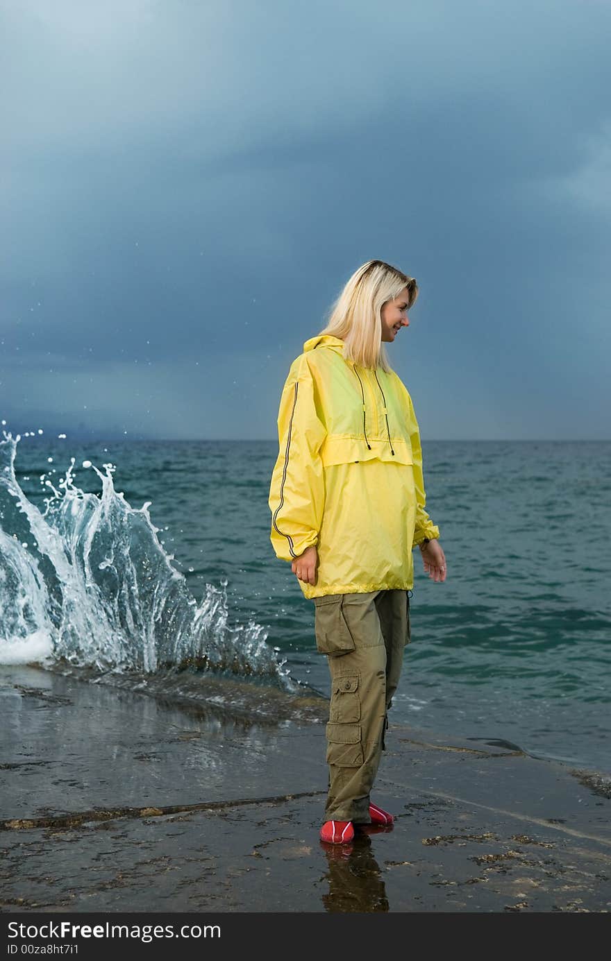 Young woman in yellow raincoat near the ocean at storm