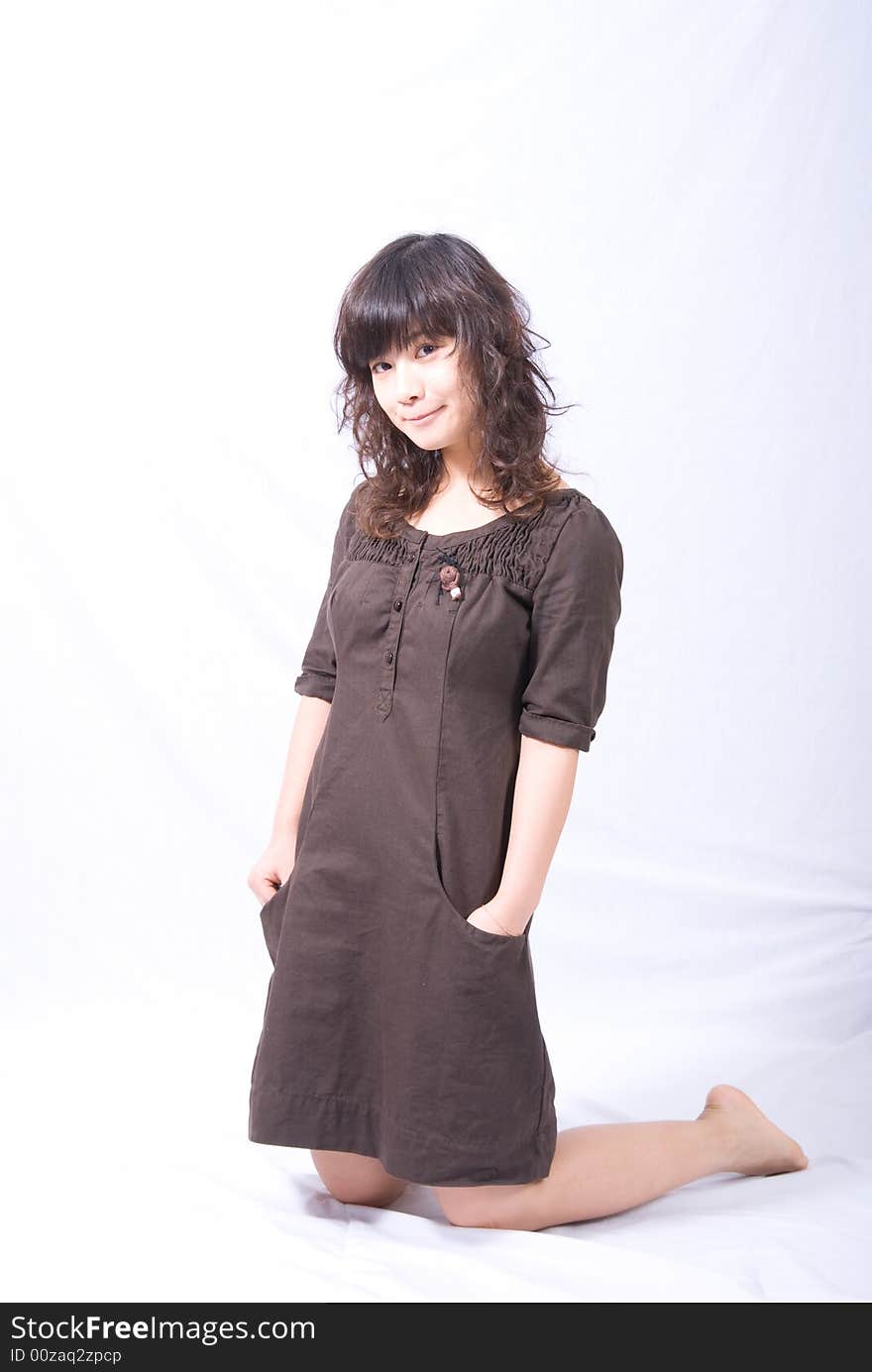 A very cute asian girl is kneeling on the white ground with a sweet smile. Dressed in a brown skirt with light brown curved hair and She looks like a doll!. A very cute asian girl is kneeling on the white ground with a sweet smile. Dressed in a brown skirt with light brown curved hair and She looks like a doll!