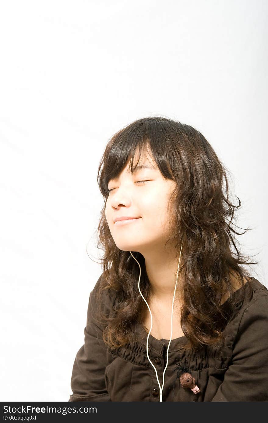 A asian female adolescent in brown skirt with light brown curved hair is enjoying the music from the white earphone. A asian female adolescent in brown skirt with light brown curved hair is enjoying the music from the white earphone