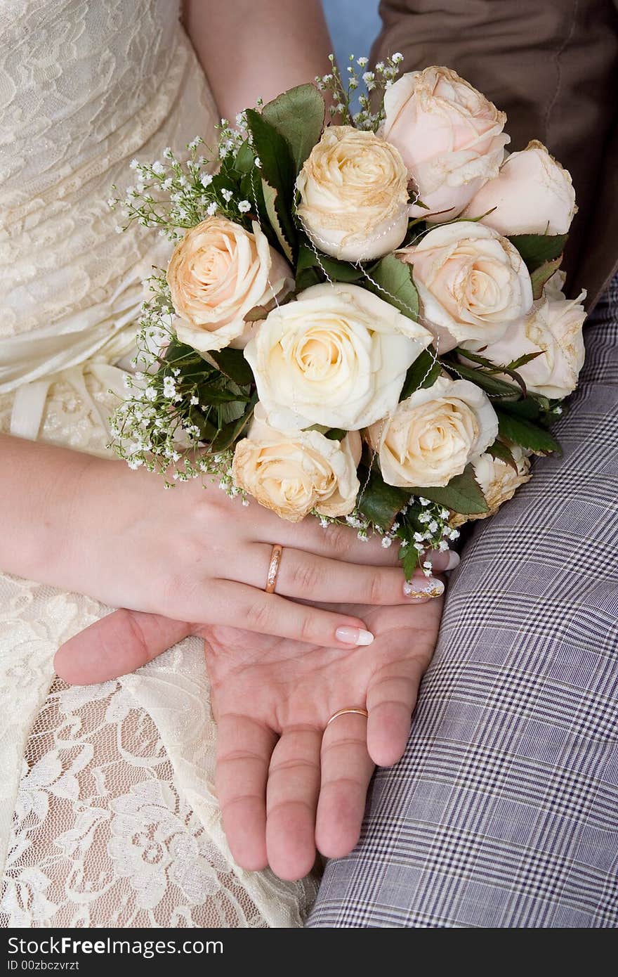 Hands of a newly-married couple with a bouquet, close up