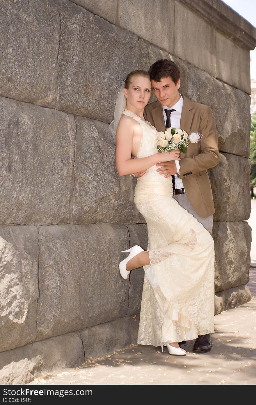 Newly-married couple near a stone wall