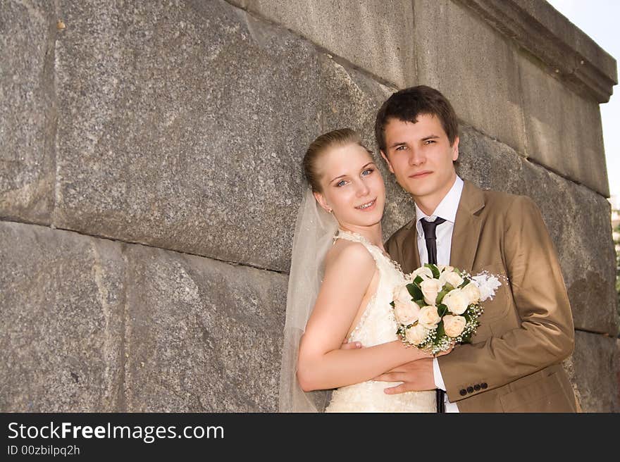 Newly-married couple near a stone wall