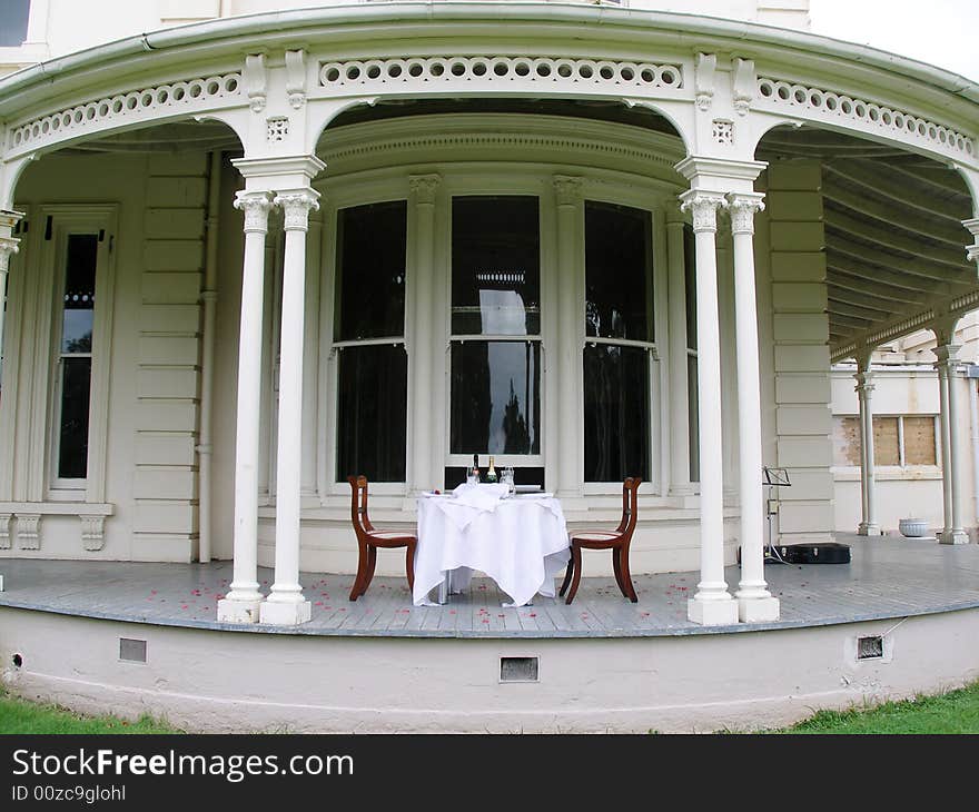 Romantic dining experience in front of antique mansion with white tablecloth, rose petals and wine. Romantic dining experience in front of antique mansion with white tablecloth, rose petals and wine.