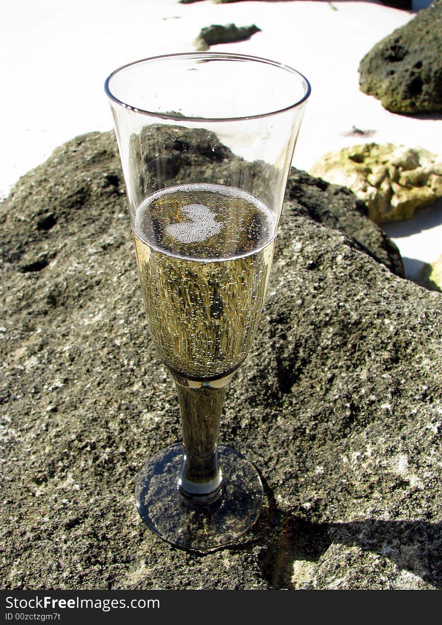 Glass of champage balancing on rocks on the beach. Glass of champage balancing on rocks on the beach