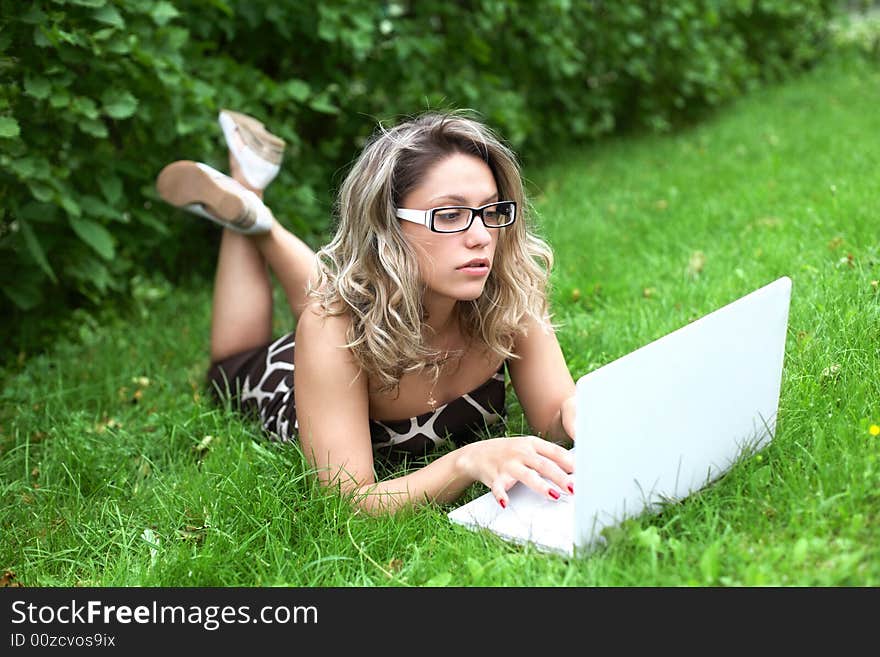 Girl with white laptop lying on green grass background. Girl with white laptop lying on green grass background