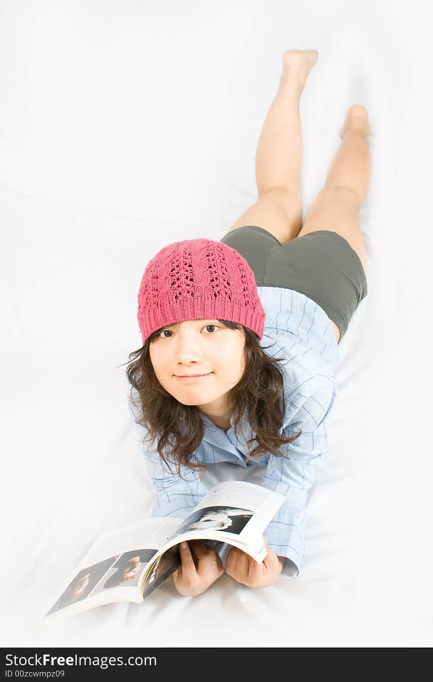 A young asian belle with knickers, light blue shirt and pink red hat is reading a magazine. A young asian belle with knickers, light blue shirt and pink red hat is reading a magazine