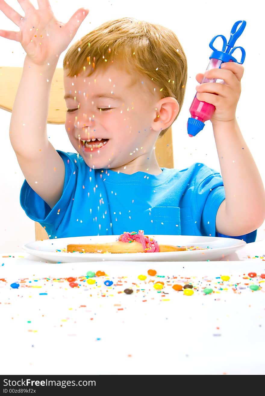 Three year old boy in blue top decorating biscuits with pink icing and sweets. Three year old boy in blue top decorating biscuits with pink icing and sweets